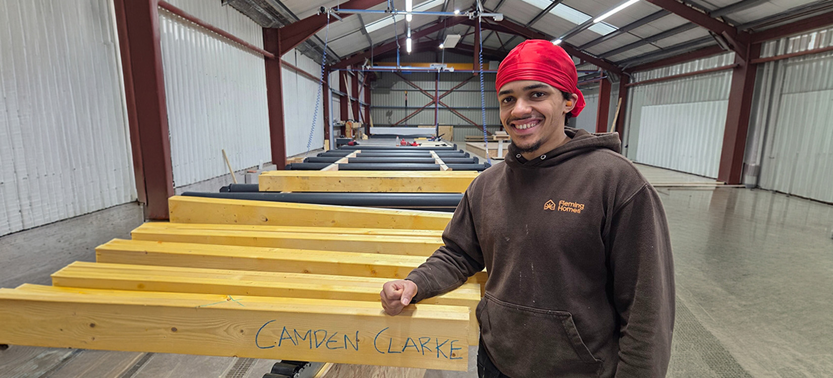Fleming Homes team member standing next to timber frame components in the workshop